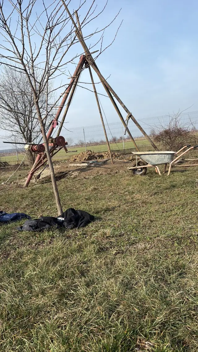 Instalație de foraj cu trepied montată pe câmp, lângă roaba cu materiale